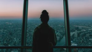 Lone woman looking out window over the city.